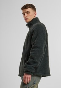 Fleece jacket in dark gray, featuring a high collar, textured surface, and side pockets. Designed for warmth and comfort.