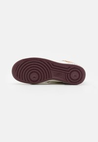 Semelle d’une chaussure Nike montrant des motifs circulaires de la bande de roulement en caoutchouc brun foncé sur fond blanc.