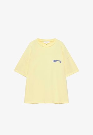 Világos sárga, rövid ujjú, kerek nyakú póló kék "OVERPACKING CREW" felirattal a bal mellkason.