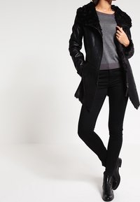 Schwarze Lederjacke mit Kunstfellkragen, offenen Vorderseite, taillierter Passform, kombiniert mit schwarzen Hosen und Stiefeletten. Glatte Textur und elegantes Design.