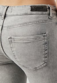 Jean en denim gris avec un gros plan de la poche arrière, présentant des coutures ton sur ton et une étiquette au niveau de la taille. Le tissu a l'air lisse et légèrement usé.