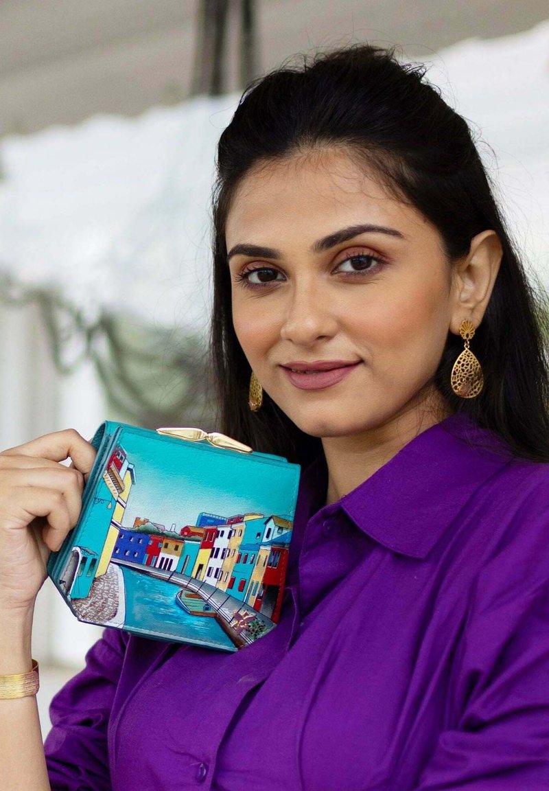 Kleurrijke rechthoekige clutch tas met een turquoise achtergrond en beschilderde gebouwen in verschillende kleuren, met een gouden sluiting.