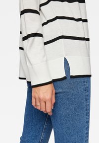 Maglione in maglia a righe bianche e nere con fondo a spacco laterale, polsini a coste e vestibilità rilassata, abbinato a jeans in denim blu.