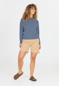 Marinblå och vit randig långärmad skjorta i kombination med beige shorts; avslappnade skor i brunt med en texturerad yta; avslappnad passform.