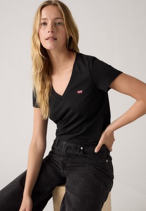 Tricou negru cu decolteu în V, fabricat din bumbac moale, având un mic logo roșu Levi's pe partea stângă a pieptului, asortat cu blugi închiși.