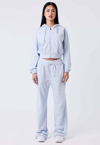 Lichtblauwe cropped hoodie met trekkoord en lange mouwen, gecombineerd met bijpassende joggingsbroek met witte piping en elastische tailleband.