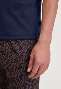 Marineblauwe T-shirt met een gladde textuur, gecombineerd met geblokte shorts met een geometrisch kubusontwerp in donkerblauw en oranje.