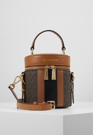 Sac à main cylindrique Michael Kors marron et noir avec fermetures éclair dorées, poignée supérieure et bandoulière amovible sur une surface blanche.