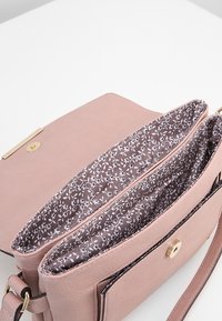 Borsa a mano rosa chiaro con rivestimento in tessuto floreale, scomparti aperti e chiusura magnetica in tono oro su una superficie bianca.