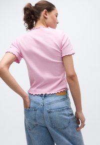Ροζ ριμπ κοντομάνικη μπλούζα με κυματιστό τελείωμα και άκρα μανικιών, σε συνδυασμό με ανοιχτό μπλε ψηλόμεσο τζιν με πίσω τσέπες.