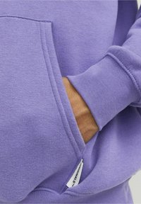 Felpa viola con tasca frontale, polsini a coste, texture morbida e etichetta al bordo della tasca.