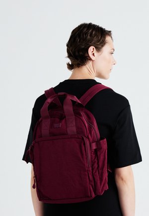 Mochila burdeos con un tejido texturizado, dos compartimentos principales con cremallera y correas de hombro acolchadas. Bolsillo frontal con detalle de cremallera.