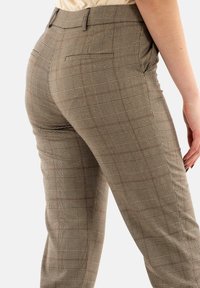 Pantalons à carreaux bruns en tissu texturé, présentant une coupe slim, des poches arrière et un motif à carreaux subtil avec des accents rouges.