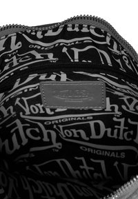 Interiér šedého látkového vaku s opakujúcim sa čiernym a bielym textovým vzorom s nápisom "Von Dutch Originals" a koženou etiketou pre branding.