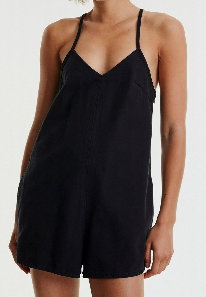 Rompers noirs avec un décolleté en V, des bretelles fines et des poches latérales. Le tissu semble lisse avec une finition légèrement mate.