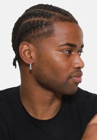 Silberne Tropfohrringe mit glänzender Oberfläche, getragen zu einer kurz geschnittenen Frisur mit dezentem Zopf, vor einem schlichten Hintergrund.