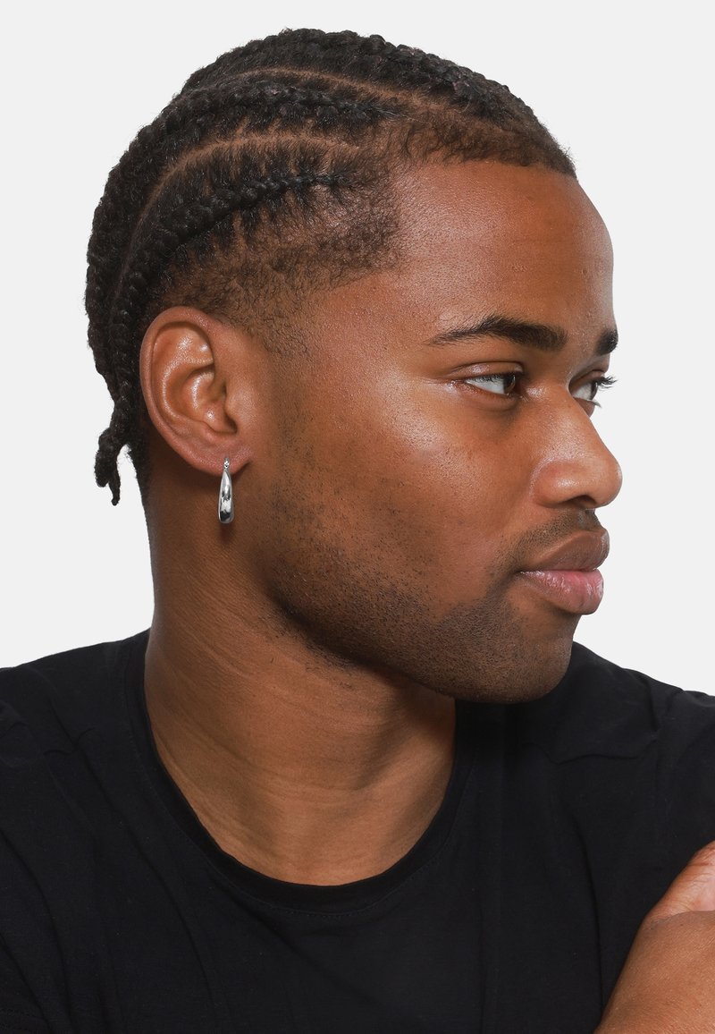 Silberne Tropfohrringe mit glänzender Oberfläche, getragen zu einer kurz geschnittenen Frisur mit dezentem Zopf, vor einem schlichten Hintergrund.