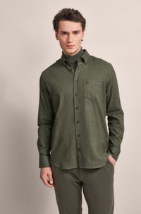 Green flannel shirt with button closure, single chest pocket, and long sleeves. Worn with a gray turtleneck and olive pants.