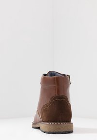 Bota de tobillo de cuero marrón con parte trasera de ante, costuras en contraste y suela de goma texturizada. Cierre de cremallera en la parte trasera para facilitar su uso.