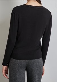 Black knit sweater with long sleeves and ribbed hem; features slight puff in shoulder seams. Paired with gray patterned trousers.
