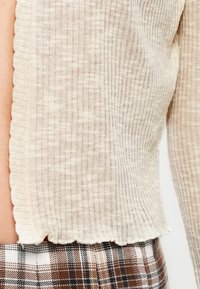 Πλεκτό μπεζ cropped τοπ με κάθετες ραβδώσεις, κυματιστό τελείωμα και απαλή υφή, συνδυασμένο με παντελόνια σε καρό καφέ και λευκό μοτίβο.