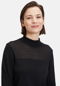 Schwarzer Pullover mit einem gerippten, gewellten Ausschnitt, transparentem oberen Bereich und solidem unteren Teil. Weiche Textur mit slim fit Design.