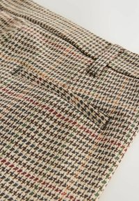Tessuto a motivo houndstooth marrone con accenti rossi e verdi; presenta una texture liscia e una tasca singola sul davanti.