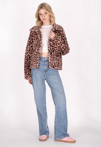Giacca in pelliccia finta con stampa leopardata e collo ampio, con tonalità di rosa e marrone, indossata sopra una maglietta bianca e abbinata a jeans azzurri chiari.