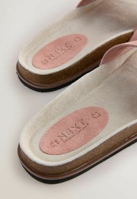 Primo piano di sandali beige chiaro con plantari sagomati, inserti ovali rosa con il marchio in rilievo e suole intermedie in sughero.