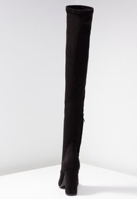 Sorte thigh-high støvler lavet af blødt, suede-lignende materiale. Blokhæl og en lynlåsdetaillinje bagpå. Glat tekstur med en tætsiddende silhuet.