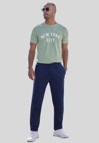Hellgrünes Baumwoll-T-Shirt mit "NEW YORK CITY" in weißen Buchstaben, kombiniert mit navyblauen Jogginghosen und weißen Turnschuhen.