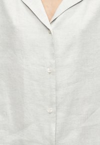 Ανοιχτό γκρι λινό πουκάμισο με γιακά με εγκοπή και τρία κουμπιά στο μπροστινό μέρος, με υφασμάτινη υφή και διακριτικές λεπτομέρειες ραφής.