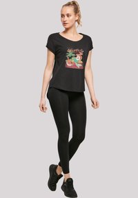 Svart grafisk t-skjorte med korte ermer og rund hals, med et fargerikt strandtema-design. Kombinert med svarte leggings og joggesko.