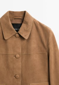 Braune Wildlederjacke mit drei stoffbezogenen Knöpfen und einem spitzen Kragen, zeigt die obere Hälfte auf einem weißen Hintergrund.