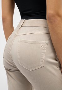 Pantalones beige de talle alto con una textura suave, que cuentan con un bolsillo trasero con un sutil acento de logo y un ligero detalle de costura.