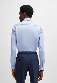 Lichtblauwe langemouwhemd met een rechte kraag, gecombineerd met donkerblauwe op maat gemaakte broeken met achterzakken en knopen.