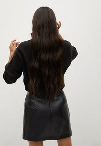 Zwarte leren mini-rok gecombineerd met een zwarte trui, met een relaxte pasvorm en lange golven van donker haar. Minimalistisch ontwerp, geen versieringen.