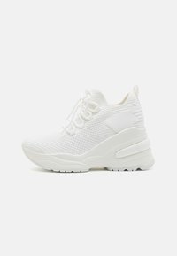 Białe sportowe sneakersy z dzianinową cholewką, grubą amortyzującą podeszwą, sznurowanym zapięciem oraz pętlą na pięcie, pokazane w profilu bocznym na białym tle.