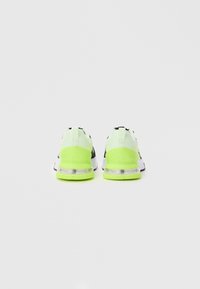 Athletic shoes with a black upper, contrasting white accents, and a bright neon green heel. Translucent soles enhance visibility and style.