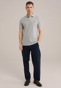 Polo gri deschis, cu mâneci scurte, guler și logo brodat pe piept, asociat cu pantaloni largi negri navy și pantofi negri.