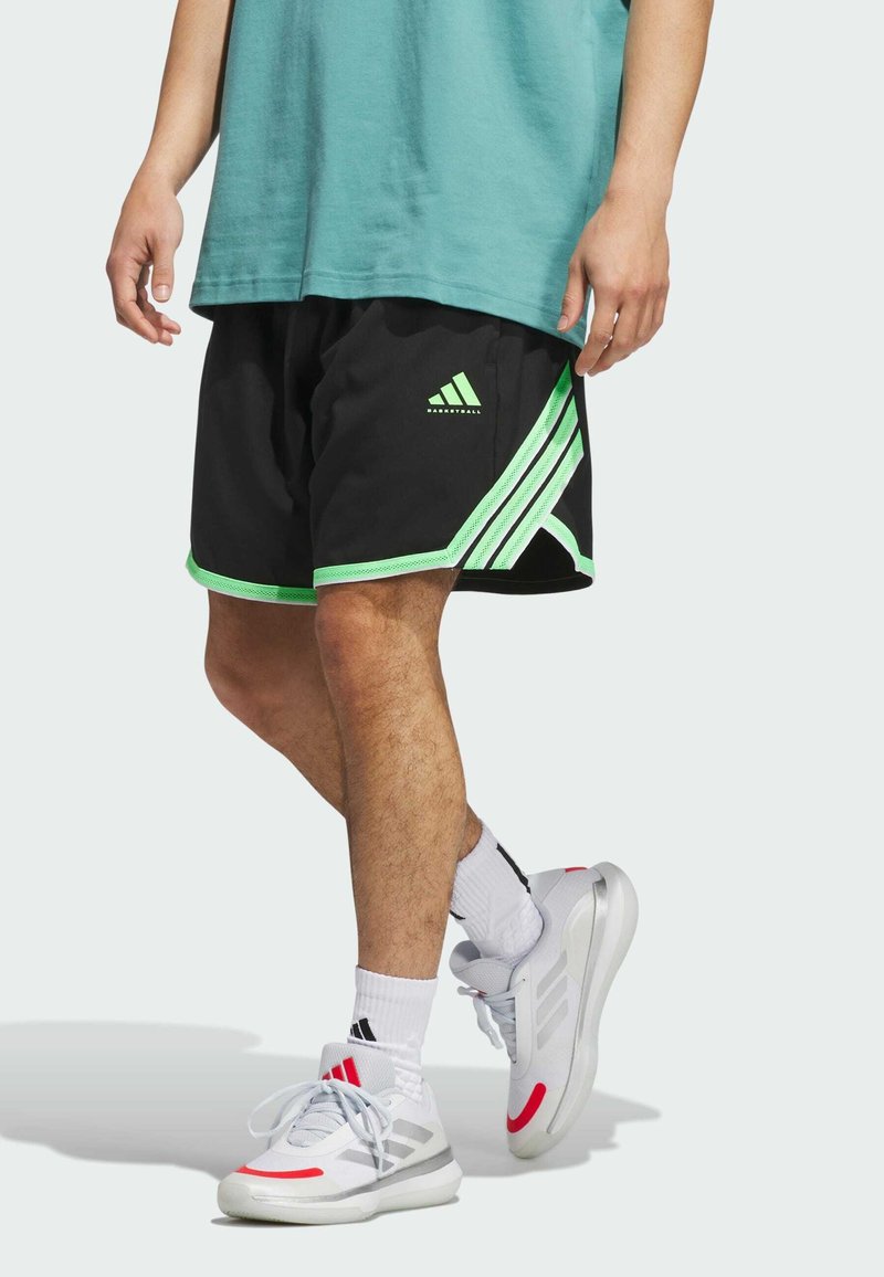 Svarta basketshorts med gröna detaljer, med en logotyp på vänster ben och tre horisontella ränder på sidorna. Bärs med vita sneakers.