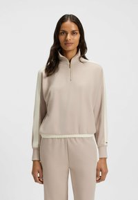 Pullover beige chiaro con colletto alto e mezza zip, caratterizzato da strisce laterali color crema e polsini elasticizzati. Tessuto morbido con una vestibilità rilassata.