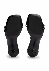 Sandali neri con tacco alto, con punte appuntite e cinturini alla caviglia. Texture liscia con finitura opaca. Le suole sono piatte con battistrada antiscivolo.