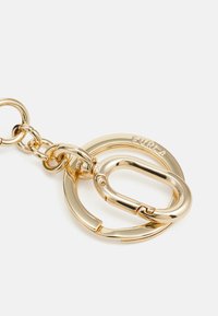 Gold-tone metal keychain featuring interlocking circular and oval shapes, a spring-loaded clasp, and engraved branding on the larger ring.