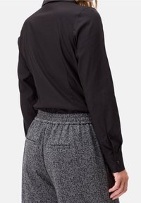 Chemise noire à manches longues associée à un pantalon gris à motif chevrons, doté d'une taille élastique et de poches arrière.