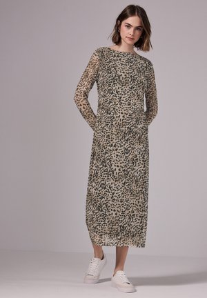 Abito trasparente a maniche lunghe di colore beige con macchie leopardate nere, caratterizzato da una linea dritta e tasche laterali, abbinato a sneakers bianche.
