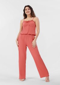 Conjunto de loungewear color coral que incluye una camiseta ajustada con bordes rizados y detalle de cordón, combinada con pantalones sueltos de pierna recta. Textura suave.