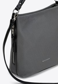 Šedá texturovaná ramenní taška s černým koženým popruhem, na přední straně má stříbrný zip a logo. Obdélníkový tvar, minimalistický design.