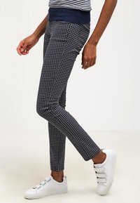 Marinblå mönstrade byxor med slim fit, med diamantformer. I kombination med vita sneakers, vilket framhäver en avslappnad och modern stil.