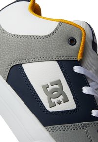 Gray and navy sneaker featuring a textured upper, white accents, yellow trim, and a logo badge. Laces are white; stitching is visible.